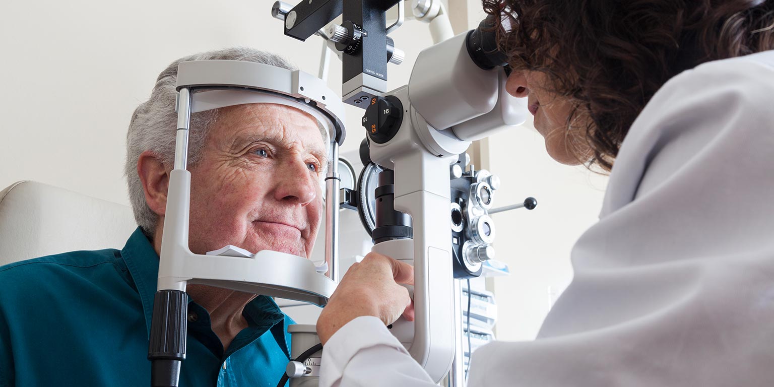 An optometry student uses a split lamp to examine an elderly patient's eyes.